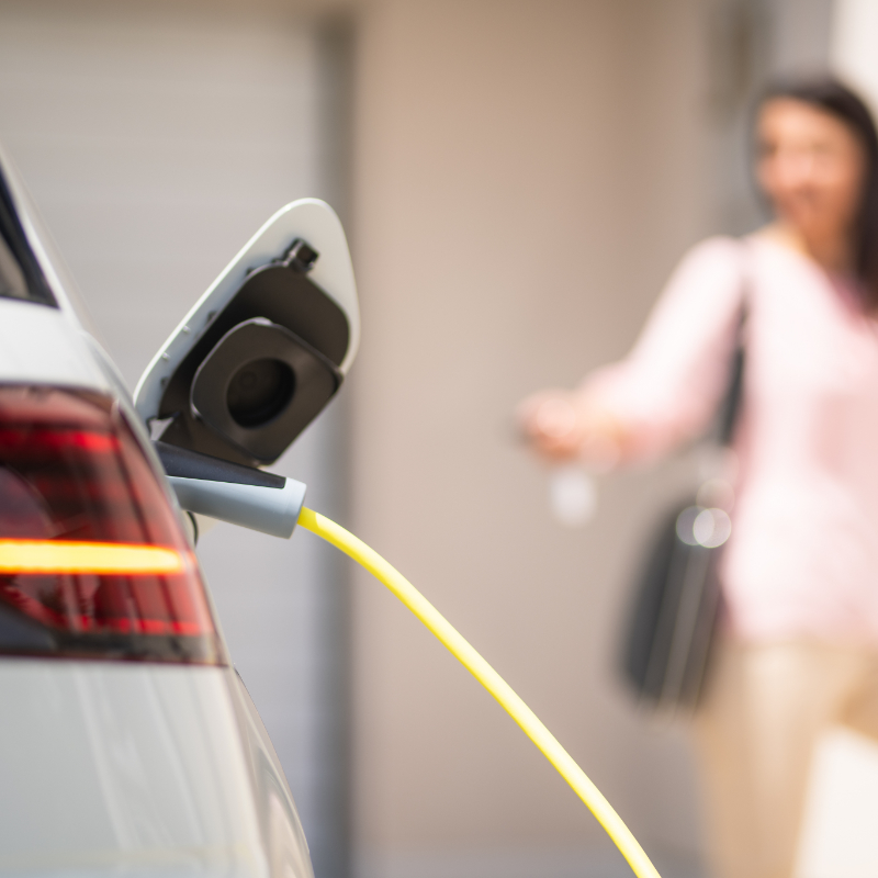 tsr - EnerConnect Close up of a electric car charger with female silhouette in the background, entering the home door and locking car