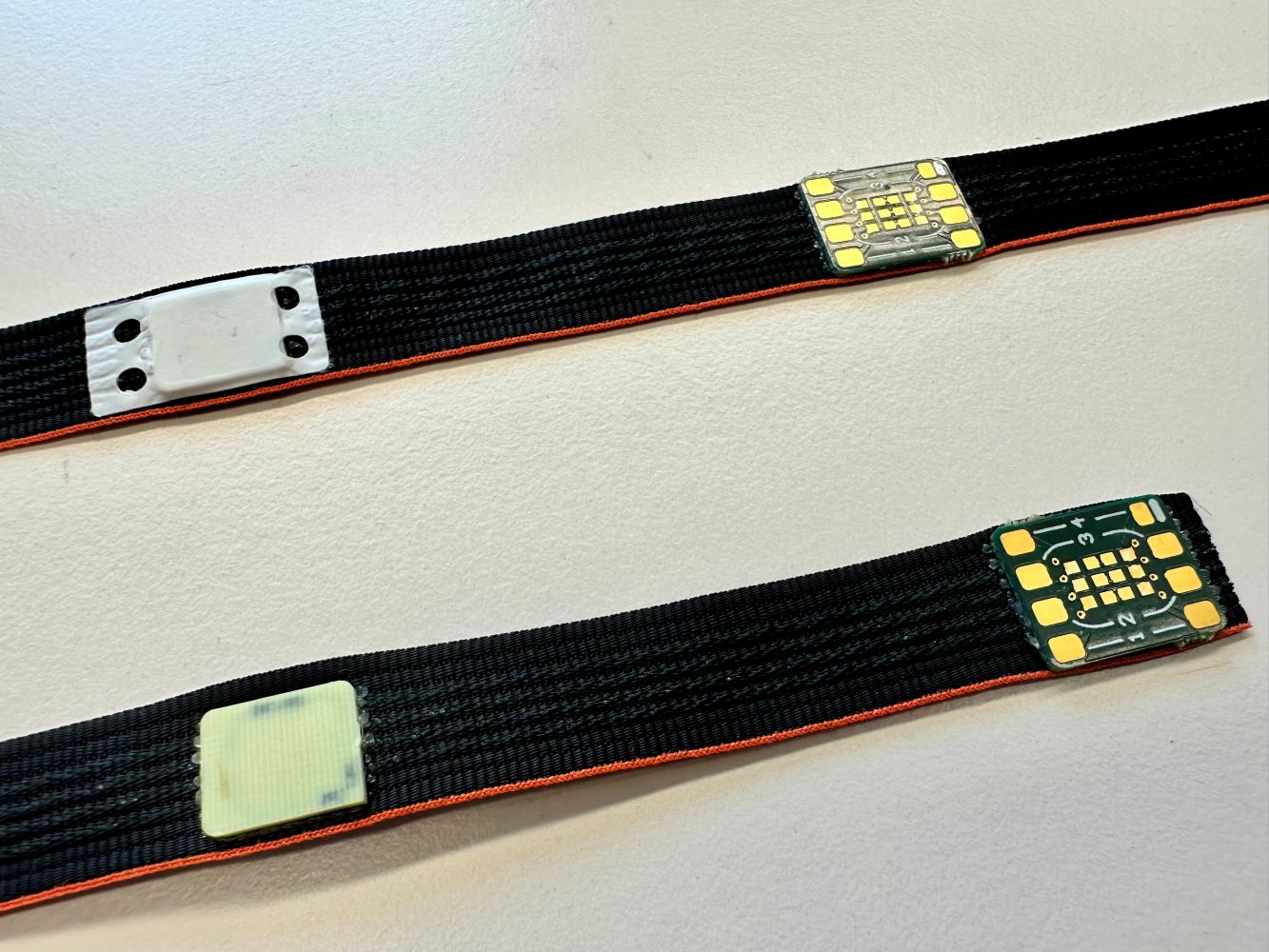 Sensormodule sind mit eingebetteten Chips und einmal blank und einmal mit zusätzlicher Barrierefolie auf leitfähige Textilbänder gebondet.