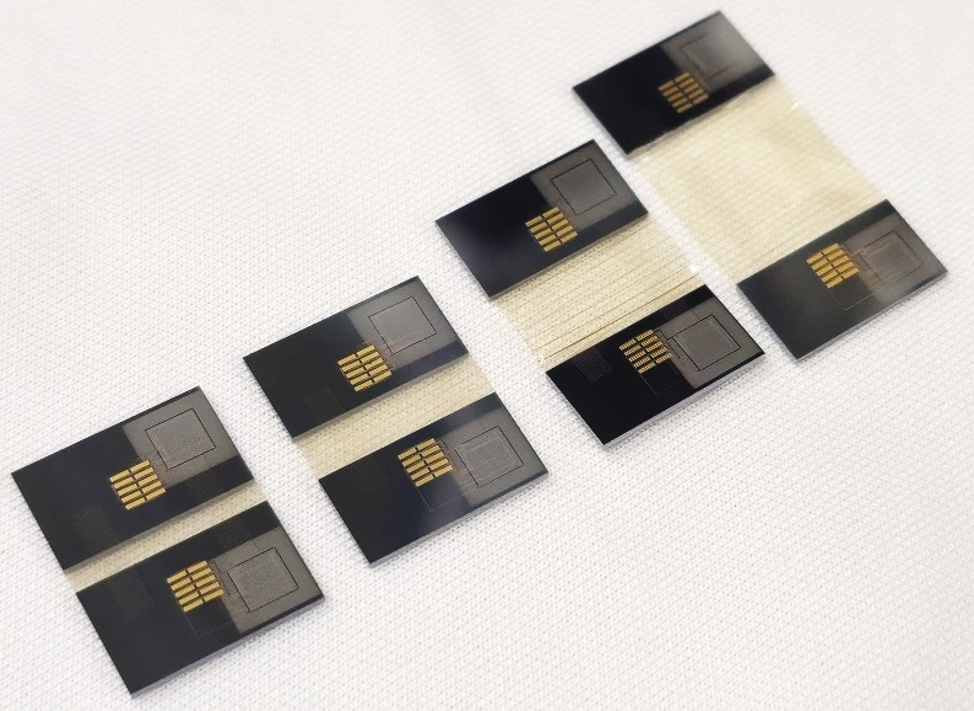 Fünf elektronische Chips auf einer weißen Oberfläche, die in zwei Gruppen angeordnet sind. / Five electronic chips arranged in two groups on a white surface.
